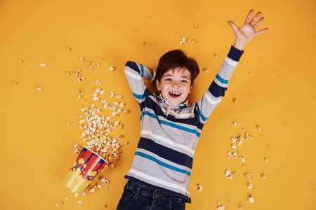 Cute little boy with popcorn lying down on the yellow floor.の写真素材