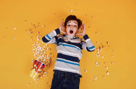 Cute little boy with popcorn lying down on the yellow floor.の写真素材