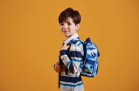 Portrait of young smart schooler in the studio against yellow background.