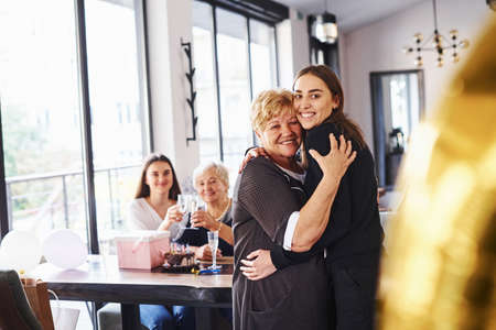Embracing each other. Senior woman with family and friends celebrating a birthday indoors.の写真素材