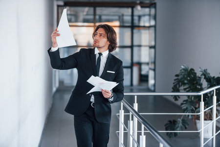 Reads documents. Portrait of handsome young businessman in black suit and tie.