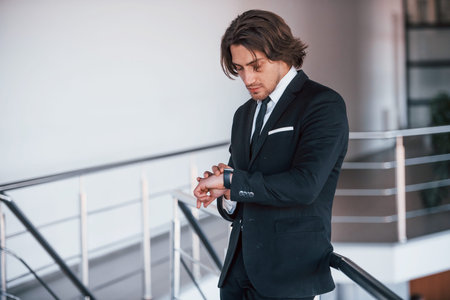 Checking time. Portrait of handsome young businessman in black suit and tie.