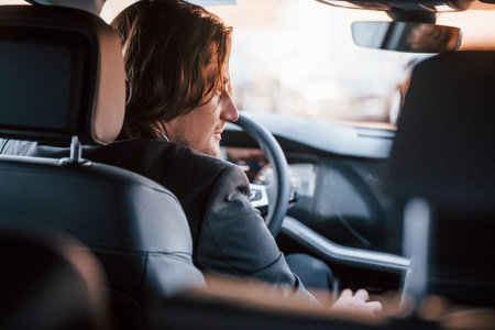 Young businessman in black suit and tie driving modern automobile.