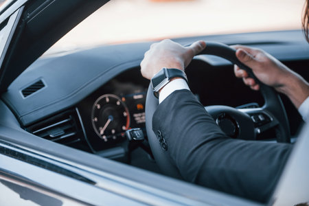 Hands of businessman in black suit and tie riding modern automobile.