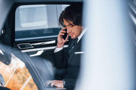 Young businessman in black suit and tie inside modern automobile.の写真素材
