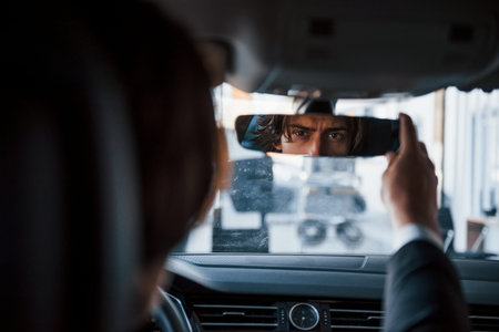 Young businessman in black suit and tie driving modern automobile.