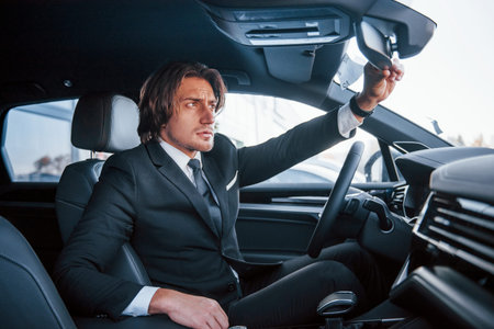 Young businessman in black suit and tie driving modern automobile.
