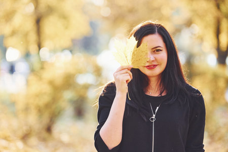 Portrait of brunette that have fun with leaves in beautiful autumn park.