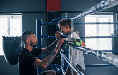 Conception of assistance. Young tattooed boxing coach teaches cute little girl in the gym.の写真素材