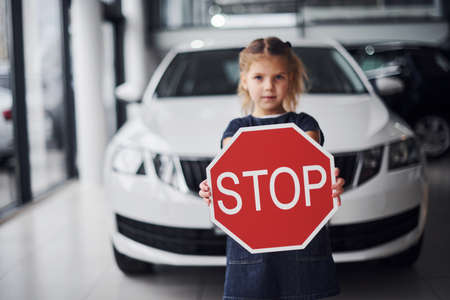 Portrait of cute little girl that holds road sign in hands in automobile salon.の写真素材