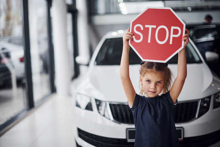 Portrait of cute little girl that holds road sign in hands in automobile salon.の写真素材