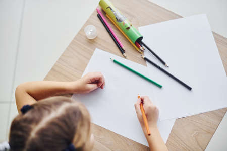 Top view of little girl with pencils and empty paper sheet on the table.の写真素材