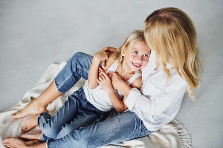 Mother with her daughter together is on the ground in the studio with white background.の写真素材