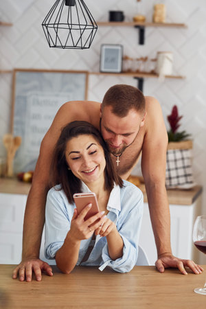Couple together in the kitchen at morning time with mobile phone.
