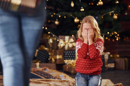 Mother standing with gift box and makes surprise for daughter indoors at christmas holidays time.