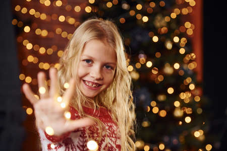 Cute little girl in near christmas tree indoors celebrating new year.の写真素材