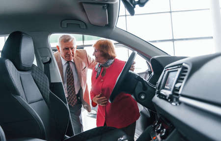 Aged man in formal wear supporting woman in choosing automobile.の写真素材