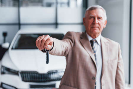 Cheerful aged man in formal wear stands in front of modern white car.の写真素材