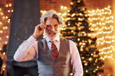 Portrait of stylish senior with grey hair and beard in jacket and white shirt is in decorated christmas room.の写真素材