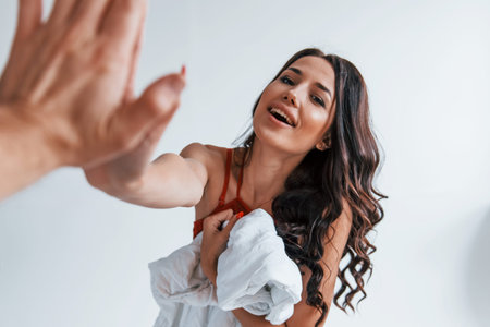Positive beautiful young brunette in underwear in white room gives high five to the other person.の写真素材