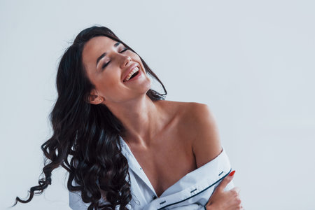Young brunette in white coat sitting on the bed in white room.