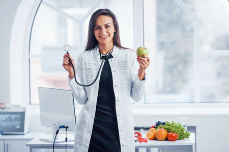 Female nutritionist in white coat sitting indoors in the office at workplace.の写真素材