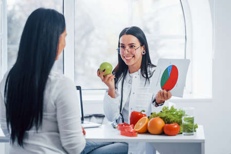 Female nutritionist with graph gives consultation to patient indoors in the office.の写真素材