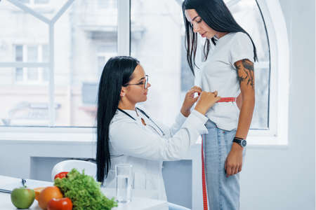 Female nutritionist measuring waist of patient by tape indoors in the office.の写真素材