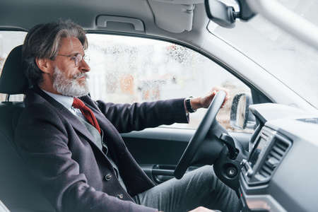 Modern stylish senior man with grey hair and mustache is in the modern car.の写真素材