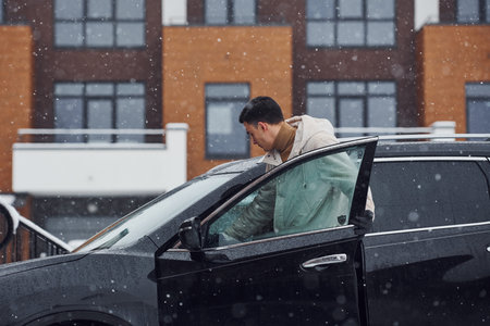 Young handsome man outdoors near his modern black car at winter time.
