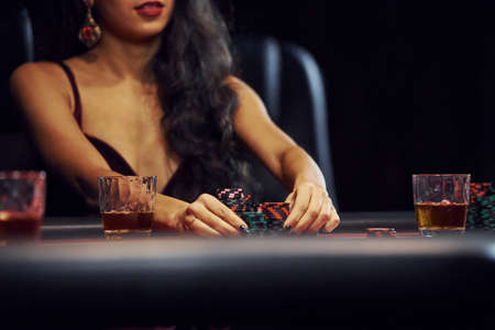 Woman in elegant clothes sits in cassino by table and plays poker game.の写真素材