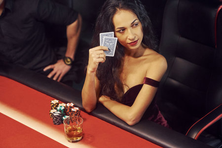 Elegant young people sits by table and playing poker in casino.