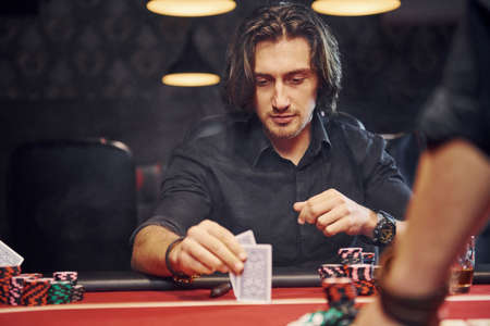 Elegant young people sits by table and playing poker in casino with smoke in the air.の写真素材