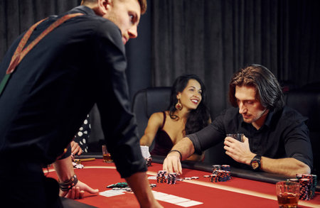 With glasses of drink. Group of elegant young people that playing poker in casino together.
