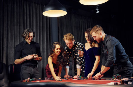 People in elegant clothes standing and playing poker in casino together.