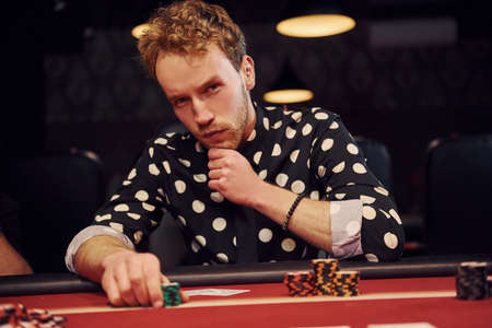 Elegant young man sits in casino and plays poker game.の写真素材