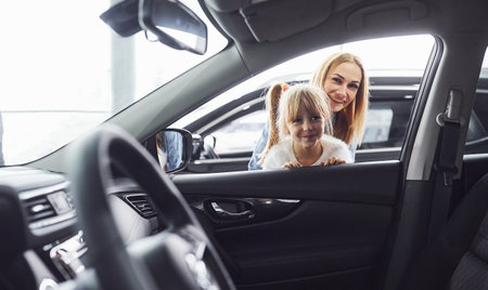 Mother and daughter looking inside modern new car in salon.