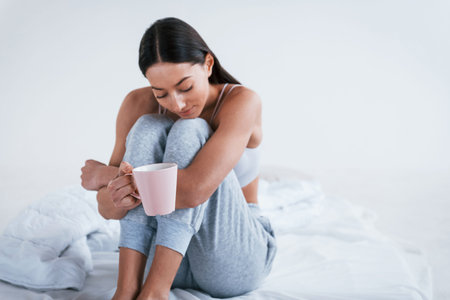 Positive smiling woman in sportive clothes sits in the studio with cup of drink.
