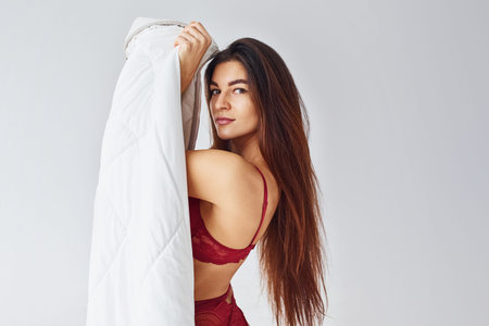 Woman in red underwear covering her body by towel in the studio against white background.の写真素材