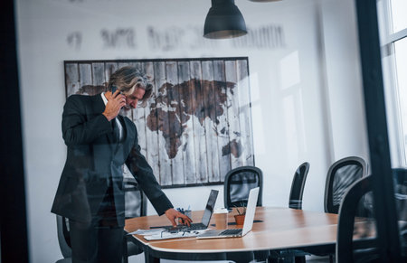 Mature businessman with grey hair and beard in formal clothes have conversation by the phone in the...