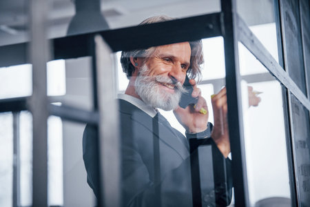 Mature businessman with grey hair and beard in formal clothes have conversation by the phone in the...