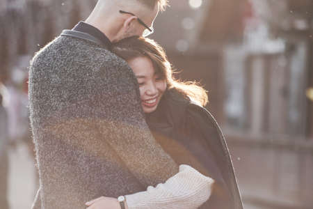 Cheerful multiracial couple embracing each other outdoors in the city. Asian girl with her caucasian boyfriend.の写真素材
