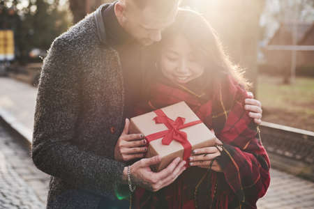 Beautiful sunlight. Happy multiracial couple together outdoors in the city with gift box in hands.の写真素材