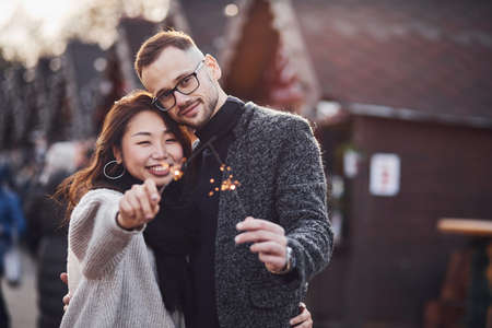 With sparklers in hands. Happy multiracial couple together outdoors in the city.の写真素材