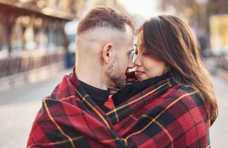 Happy multiracial couple warming up by red plaid together outdoors in the city.の写真素材