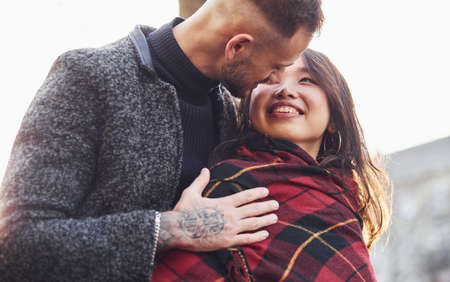 Happy multiracial couple warming up by red plaid together outdoors in the city.の写真素材