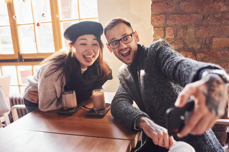 Multiracial couple making selfie in cafe. Asian girl with her caucasian boyfriend.