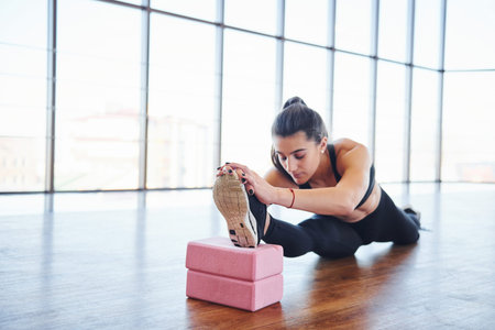 Beautiful sporty woman in sportswear doing stretching by using equipment on the floor.