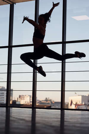 Silhouette of young sporty woman in sportswear that doing acrobatic tricks in the gym.の写真素材