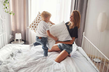Mother playing pillow fight with her son in bedroom at daytime.の写真素材